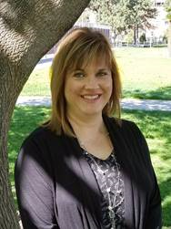Image of Shawna Hanson, woman in black top and blonde hair, standing in front of a tree.