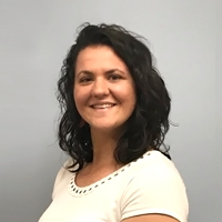 Headshot of Sarah with brown curly hair smiling wearing a white shirt