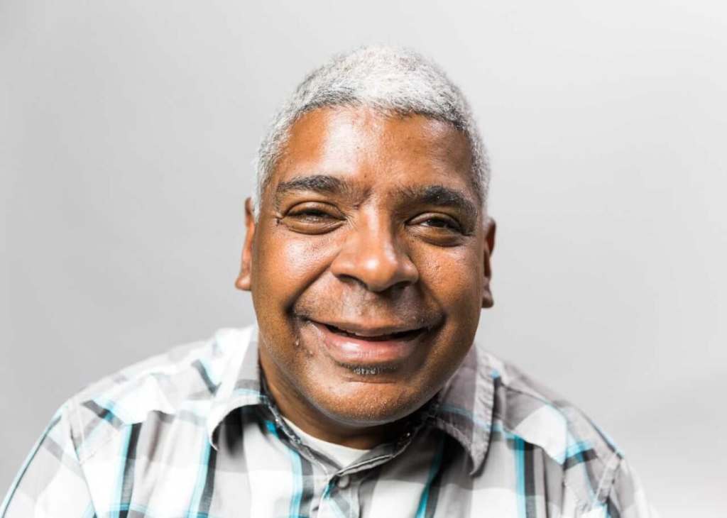 Headshot of Joe Basey, male of color with white hair and a plaid shirt