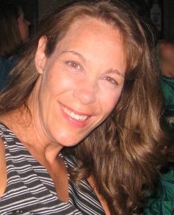 Headshot of Julie - white woman smiling at the camera with light brown hair and striped shirt.