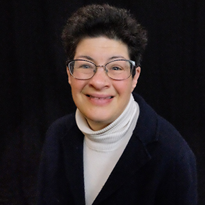 Image of Liz a white woman with an intellectual and developmental disability is smiling wearing glasses. 