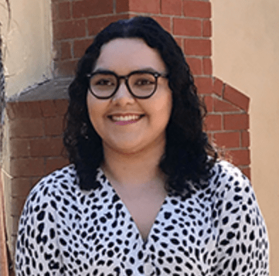 A color photo of Shirley standing in front of a brick wall.