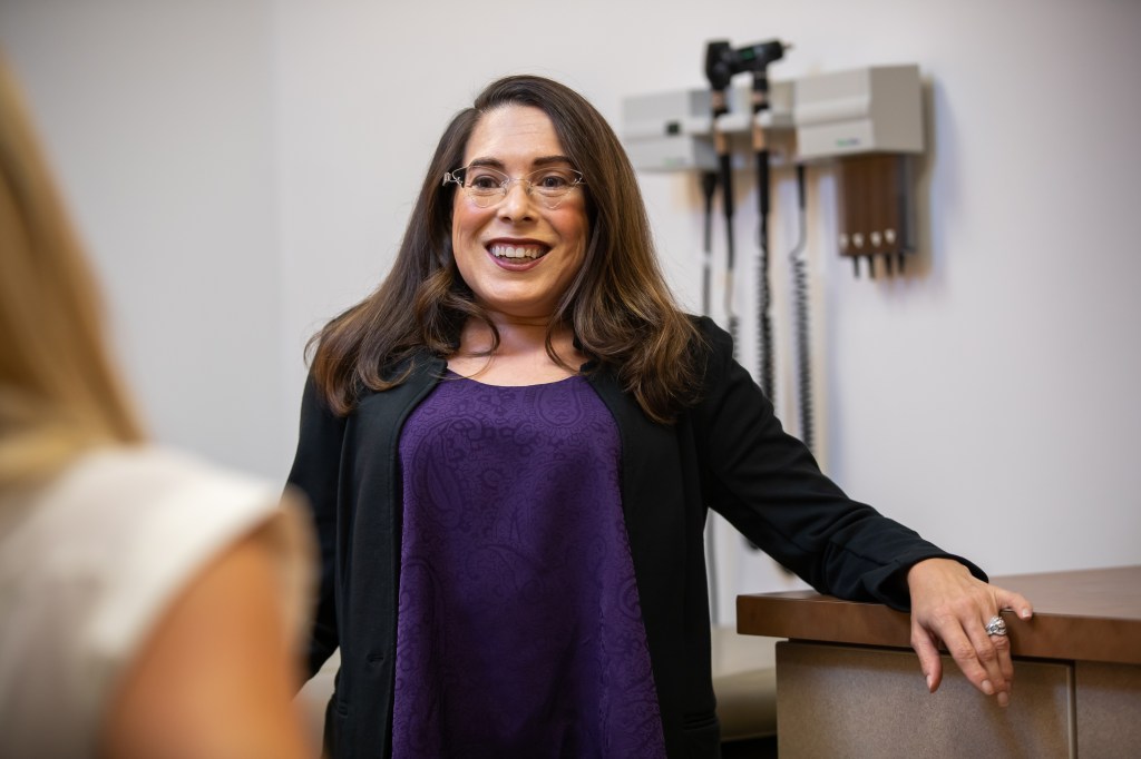 picture of the author, Amy Houtrow, in a purple shirt and black sweater in a doctor's office