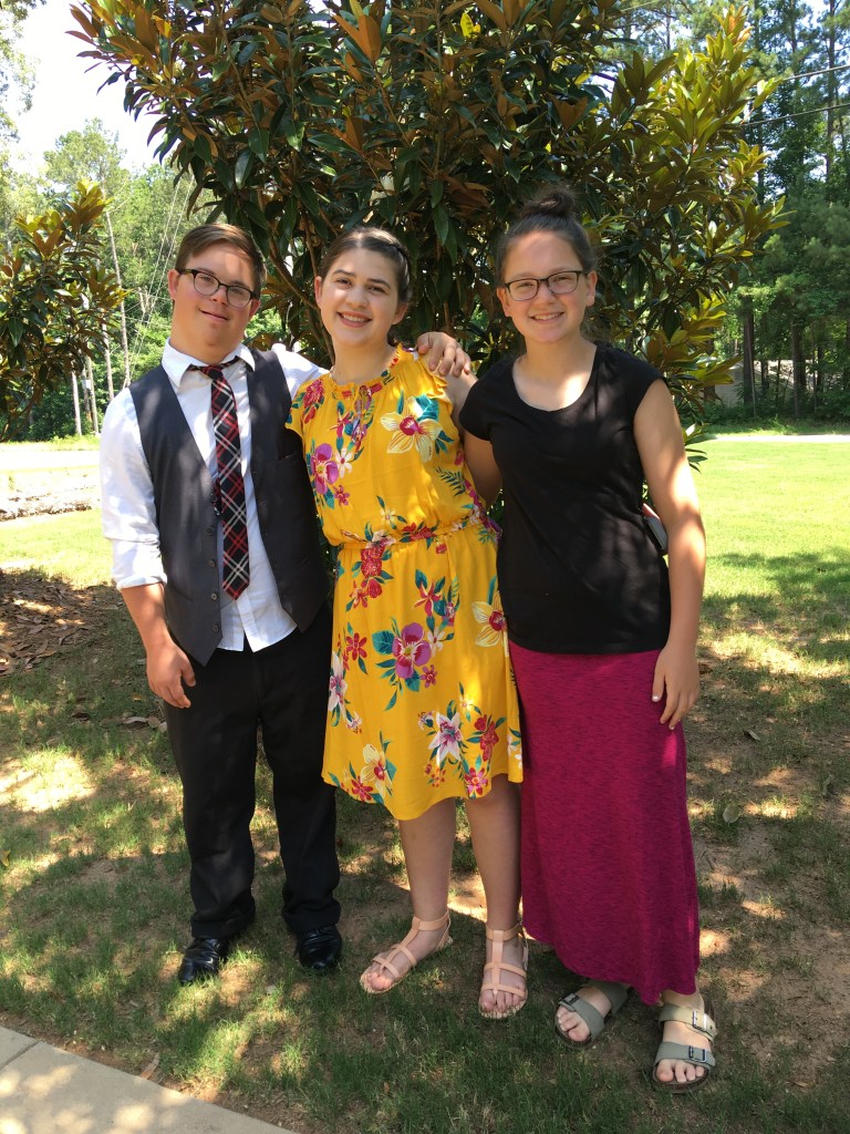Andy, Kate, and Lily Meredith stand together outside with trees and grass in the background.